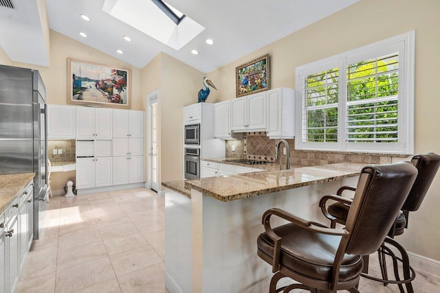 kitchen featuring a skylight, stone counters, light tile floors, and appliances with stainless steel finishes