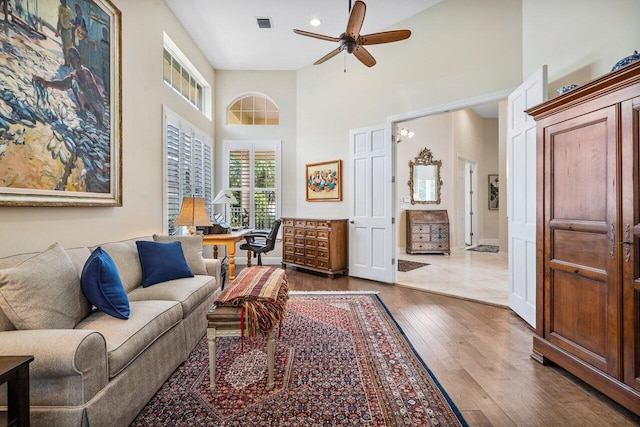 living room with ceiling fan, dark wood-type flooring, and a towering ceiling