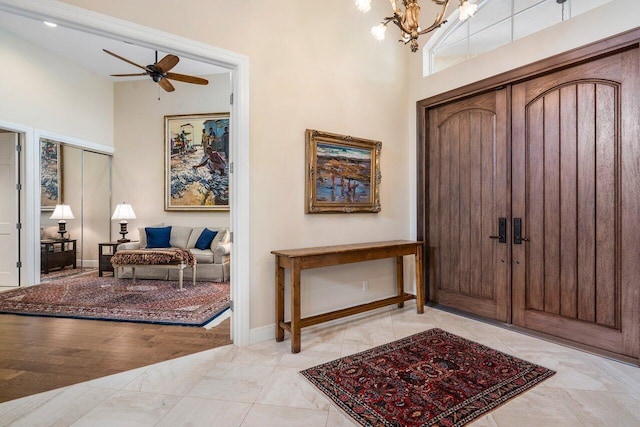 tiled entryway with ceiling fan with notable chandelier and a high ceiling