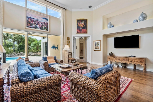 living room with plenty of natural light, light hardwood / wood-style floors, a towering ceiling, and ornamental molding