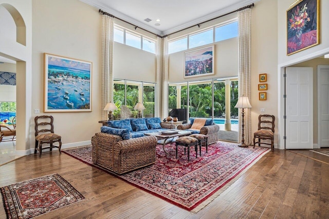 living room with plenty of natural light, ornamental molding, dark wood-type flooring, and a towering ceiling