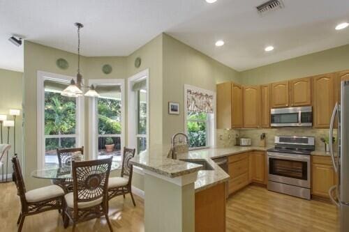 kitchen with stainless steel appliances, hanging light fixtures, kitchen peninsula, light stone counters, and sink