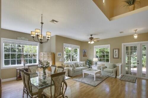 dining room with ceiling fan with notable chandelier, french doors, a wealth of natural light, and light hardwood / wood-style floors