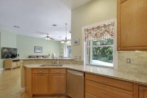 kitchen featuring light stone countertops, kitchen peninsula, ceiling fan, sink, and stainless steel dishwasher