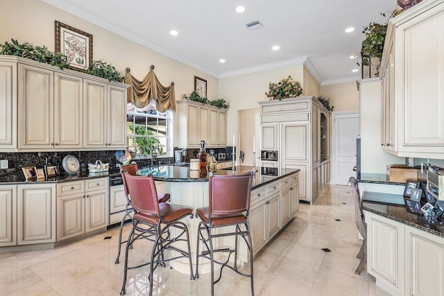 kitchen featuring backsplash, ornamental molding, cream cabinetry, and a kitchen breakfast bar