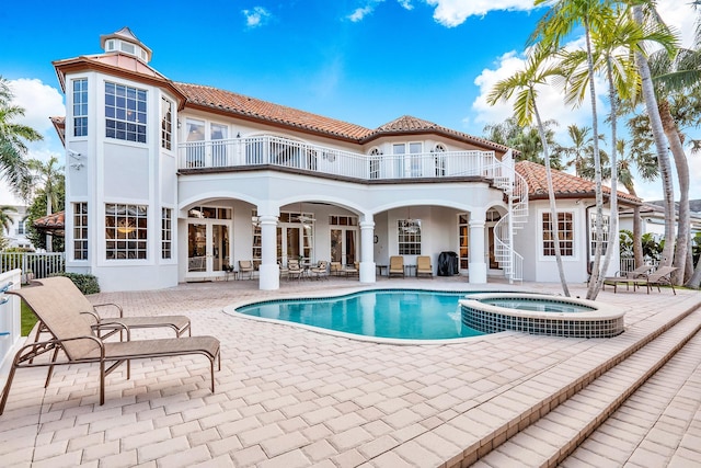 rear view of property featuring french doors, a pool with hot tub, a balcony, and a patio area