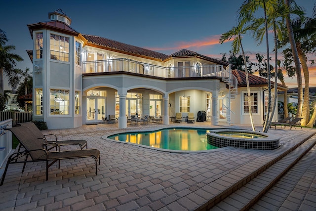 back house at dusk with a balcony, a swimming pool with hot tub, and a patio area