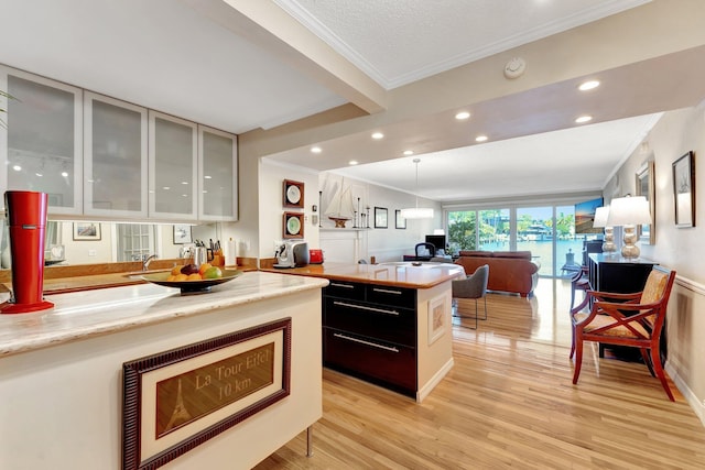 kitchen with crown molding, a kitchen island, decorative light fixtures, and light hardwood / wood-style flooring