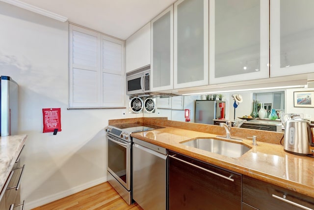 kitchen featuring sink, appliances with stainless steel finishes, white cabinetry, light stone counters, and light wood-type flooring