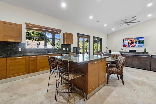 kitchen with backsplash, a breakfast bar area, ceiling fan, and light tile floors