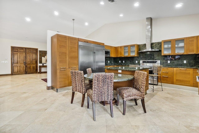 kitchen featuring a kitchen bar, light tile floors, stainless steel built in fridge, wall chimney range hood, and stove