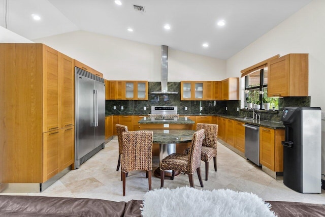 kitchen featuring stainless steel appliances, light tile floors, wall chimney range hood, backsplash, and dark stone countertops