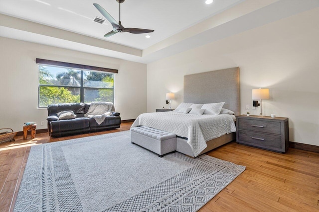 bedroom featuring a tray ceiling, ceiling fan, and light wood-type flooring