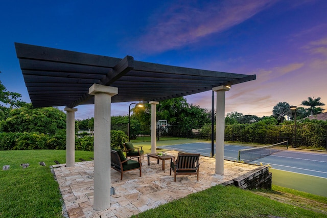 patio terrace at dusk with tennis court, a pergola, and a lawn