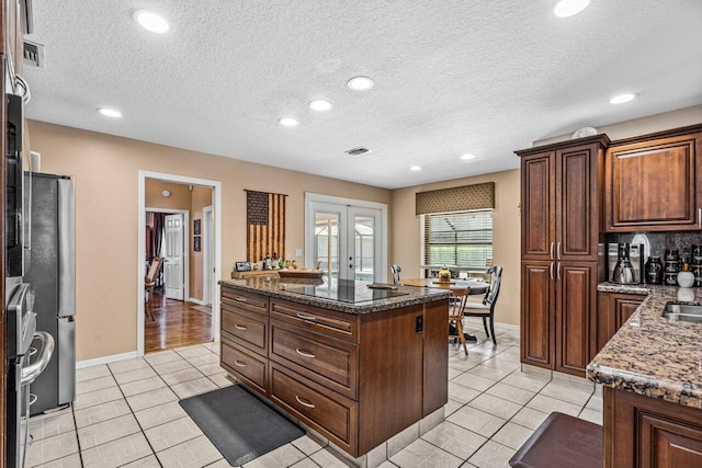 kitchen featuring french doors, an island with sink, light tile floors, a textured ceiling, and black electric stovetop