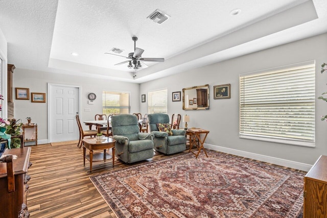 living room featuring dark wood-type flooring, a textured ceiling, ceiling fan, and a tray ceiling