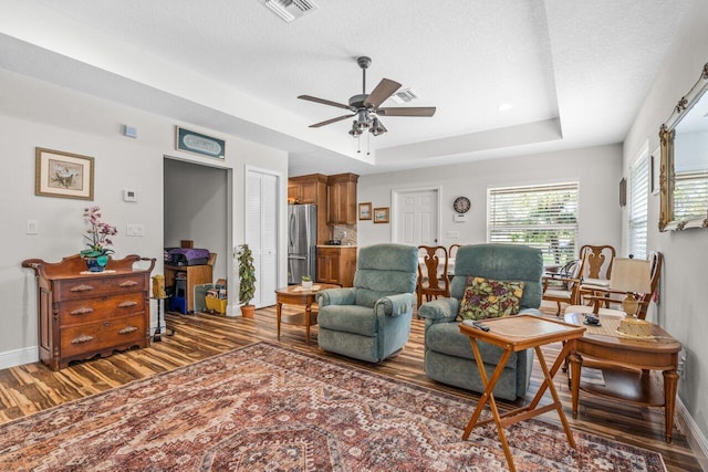 living room featuring a raised ceiling, dark hardwood / wood-style flooring, a textured ceiling, and ceiling fan