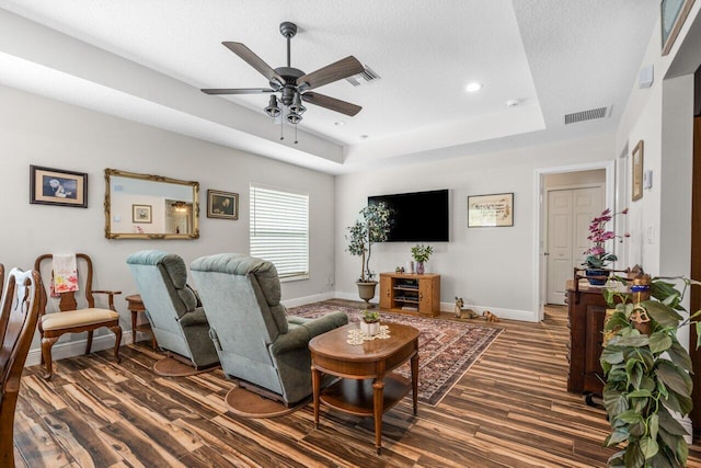 living room with a raised ceiling, ceiling fan, a textured ceiling, and dark hardwood / wood-style flooring