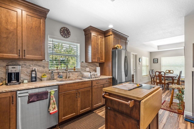 kitchen featuring light stone countertops, backsplash, appliances with stainless steel finishes, light hardwood / wood-style floors, and sink