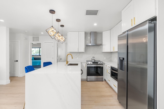 kitchen with light hardwood / wood-style floors, tasteful backsplash, wall chimney range hood, sink, and appliances with stainless steel finishes