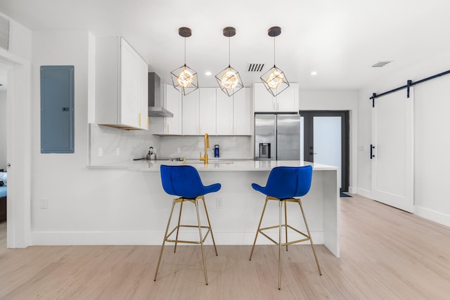 kitchen with wall chimney range hood, stainless steel fridge with ice dispenser, light wood-type flooring, decorative light fixtures, and tasteful backsplash