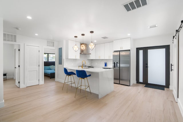 kitchen with light hardwood / wood-style floors, stainless steel fridge, a barn door, backsplash, and white cabinets