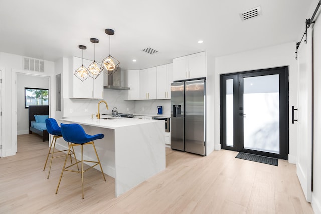 kitchen featuring light hardwood / wood-style flooring, wall chimney exhaust hood, stainless steel fridge, a barn door, and white cabinets