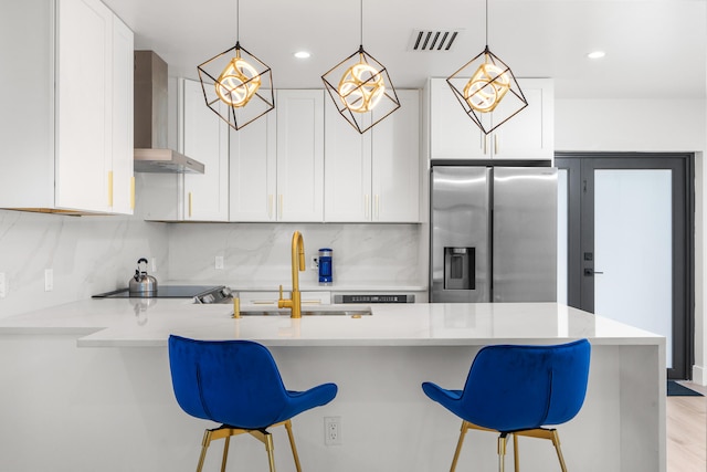 kitchen with light hardwood / wood-style floors, backsplash, stainless steel fridge with ice dispenser, wall chimney range hood, and white cabinetry