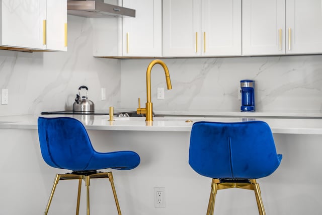 kitchen with a breakfast bar, white cabinetry, and backsplash