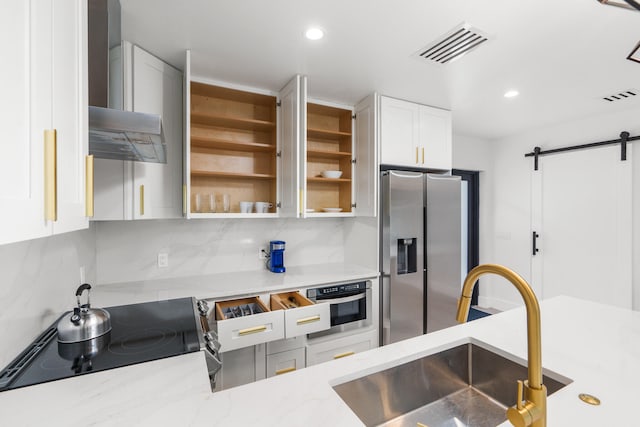 kitchen featuring appliances with stainless steel finishes, wall chimney exhaust hood, backsplash, a barn door, and sink