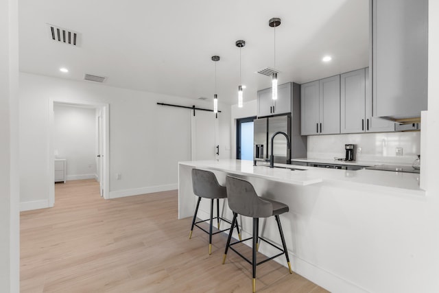 kitchen with tasteful backsplash, light wood-type flooring, pendant lighting, a barn door, and stainless steel fridge with ice dispenser