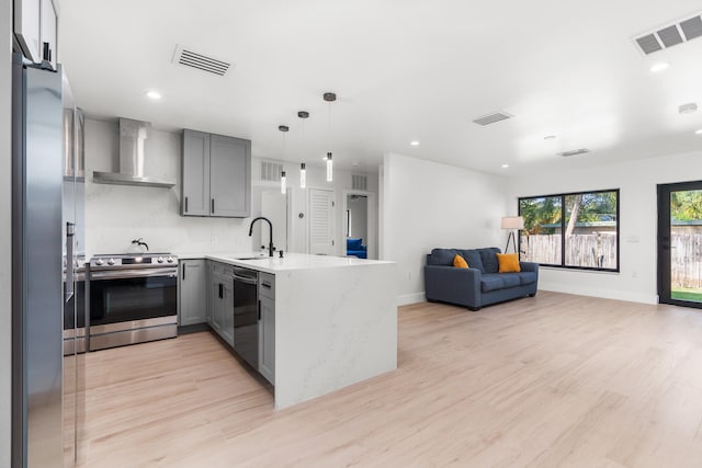 kitchen featuring kitchen peninsula, wood-type flooring, gray cabinets, wall chimney exhaust hood, and appliances with stainless steel finishes