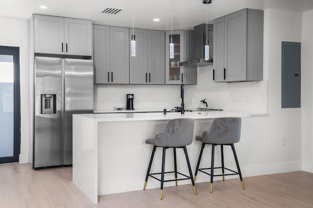 kitchen with light hardwood / wood-style floors, hanging light fixtures, kitchen peninsula, wall chimney exhaust hood, and stainless steel refrigerator with ice dispenser