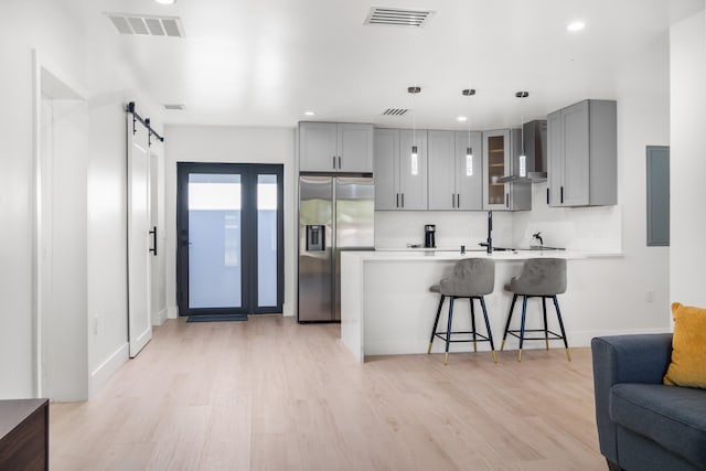 kitchen with stainless steel fridge with ice dispenser, light wood-type flooring, kitchen peninsula, wall chimney exhaust hood, and a barn door