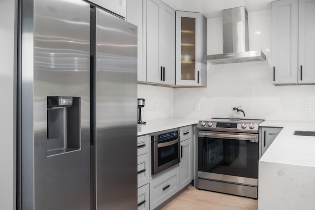 kitchen with appliances with stainless steel finishes, light hardwood / wood-style flooring, wall chimney range hood, and gray cabinets