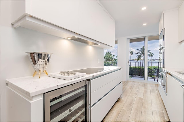 kitchen featuring light stone countertops, wine cooler, light hardwood / wood-style flooring, black electric stovetop, and white cabinets