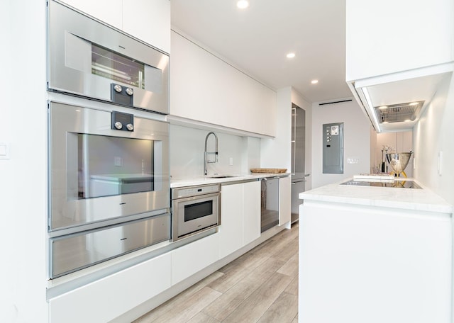 kitchen with white cabinets, oven, light hardwood / wood-style floors, and sink