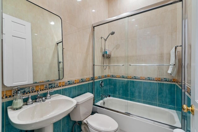 full bathroom with toilet, bath / shower combo with glass door, tile walls, and sink