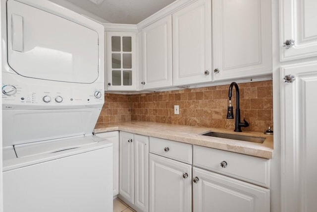 clothes washing area featuring stacked washing maching and dryer, sink, light tile patterned floors, and cabinets