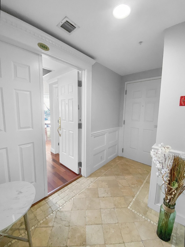 hall featuring visible vents, a decorative wall, and wainscoting