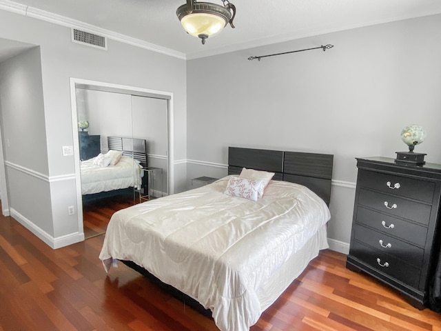 bedroom with wood finished floors, visible vents, baseboards, ornamental molding, and a closet