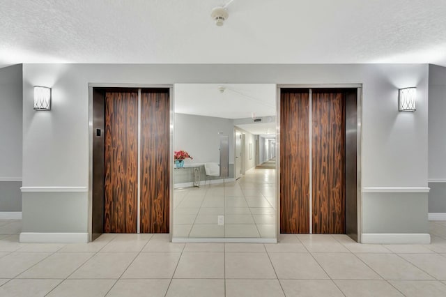 hallway featuring elevator, a textured ceiling, and light tile patterned flooring