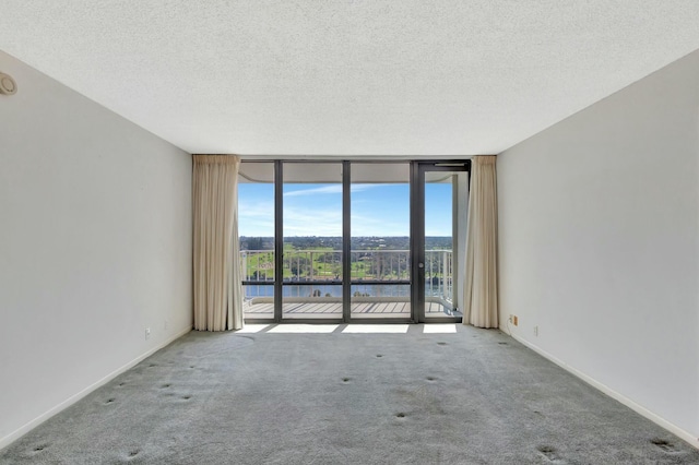 carpeted empty room featuring floor to ceiling windows, a water view, and a textured ceiling