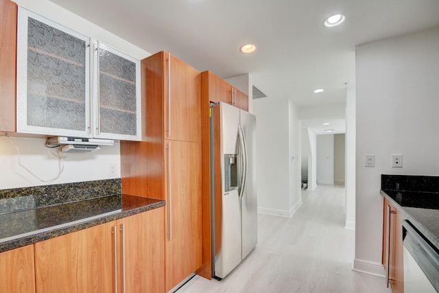 kitchen featuring stainless steel fridge, dishwasher, dark stone counters, and light wood-type flooring