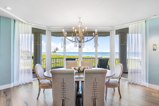 dining area with an inviting chandelier, a wall of windows, a water view, and light hardwood / wood-style flooring