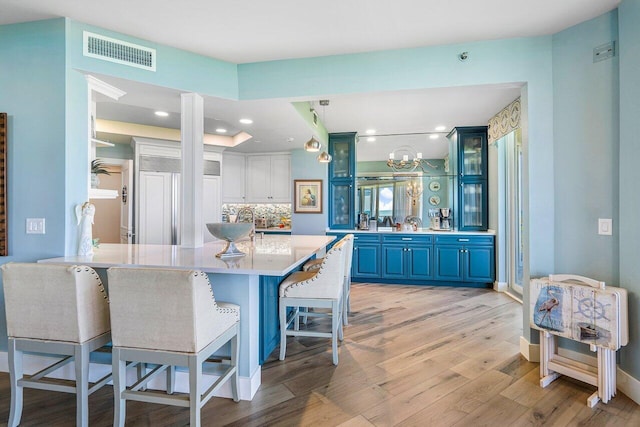 kitchen featuring blue cabinets, pendant lighting, light hardwood / wood-style floors, tasteful backsplash, and a kitchen bar