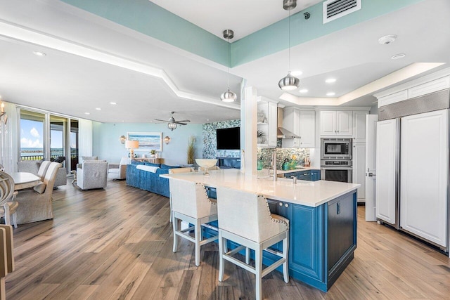 kitchen featuring ceiling fan, white cabinets, built in appliances, a breakfast bar area, and pendant lighting