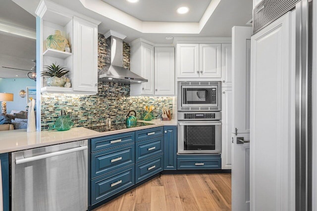 kitchen featuring backsplash, stainless steel appliances, light wood-type flooring, blue cabinetry, and wall chimney range hood