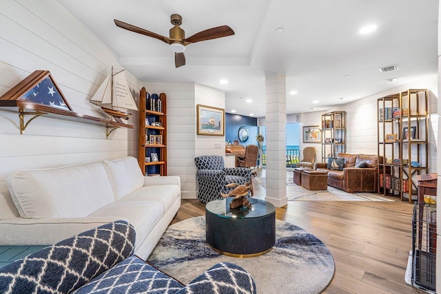 living room featuring light wood-type flooring, ceiling fan, and ornate columns