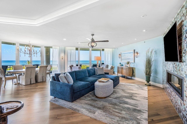 living room with a stone fireplace, light hardwood / wood-style floors, ceiling fan with notable chandelier, and a water view